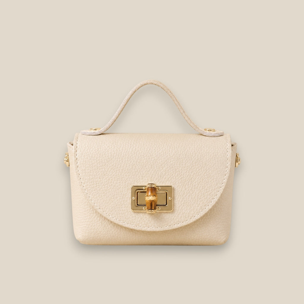 Bolso de piel crema con solapa redondeada, broche metálico dorado y detalle central de bambú