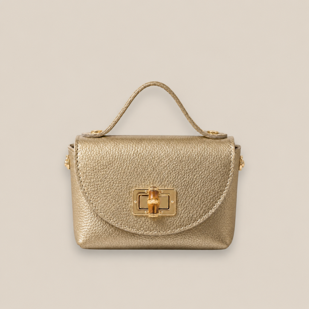 Bolso de piel dorado con solapa redondeada, broche metálico dorado y detalle central de bambú
