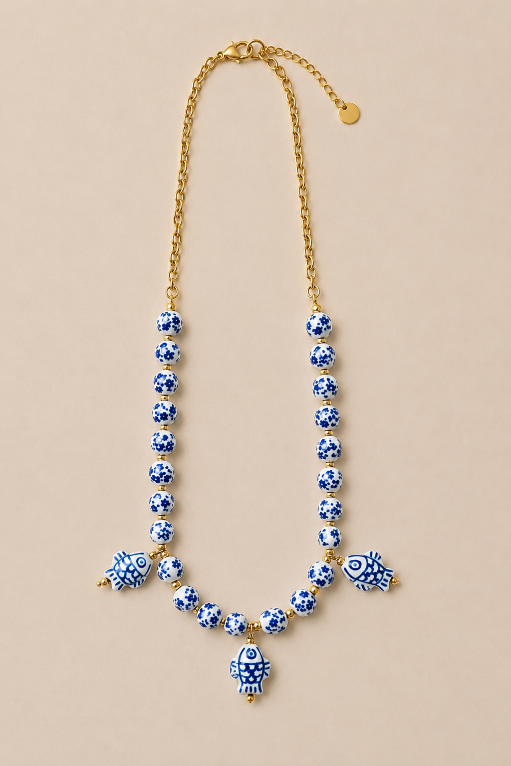 Collar de cuentas de porcelana azul y blanca con detalles y colgante de pez en acero inoxidable dorado.