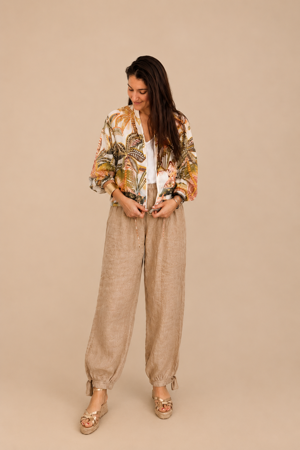 Modelo con chaqueta estampada tropical y pantalón bombacho de lino beige, posando en un ambiente minimalista de tonos neutros con decoración