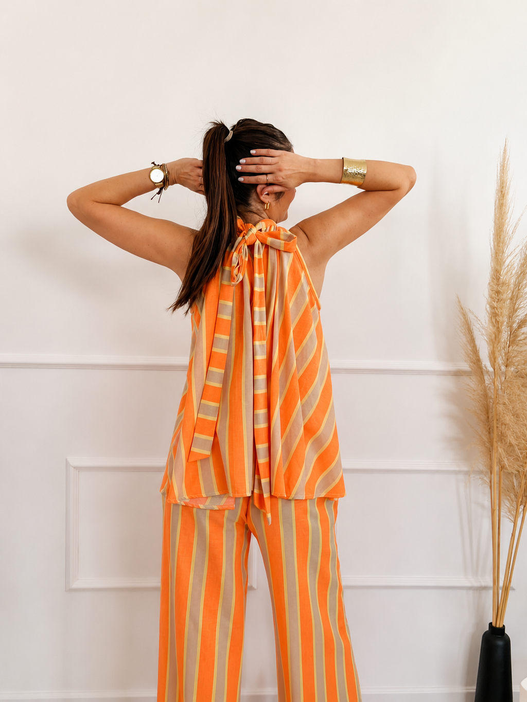 Modelo con el Conjunto Bali de rayas naranja y arena, mostrando la lazada del top halter en la espalda, pantalón ancho con bolsillos