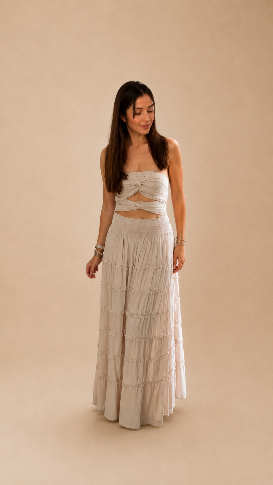 Modelo vistiendo el Vestido Gala marron chocolate, diseño strapless con nudo frontal y falda larga escalonada con volantes en algodón natural.