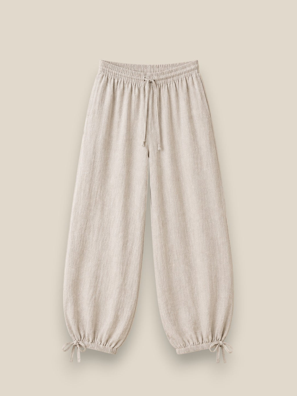 Pantalón bombacho de lino en color beige topo con cintura elástica, lazadas ajustables en el bajo y tejido ligero de estilo mediterráneo